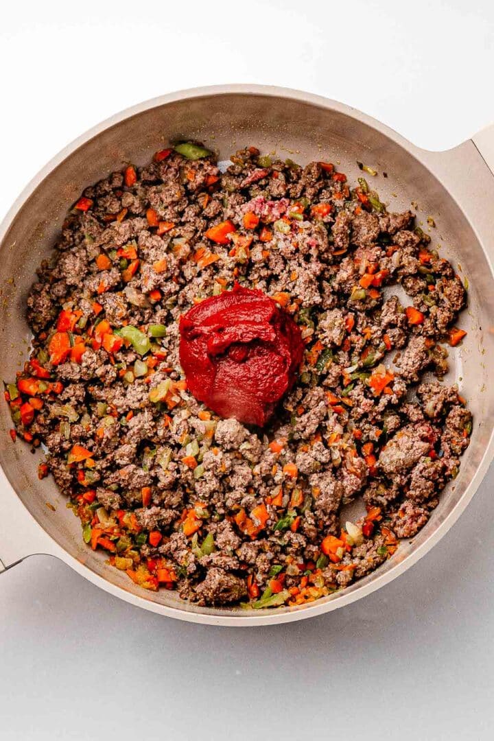Tomato paste stirred into browned ground beef, darkening in the pot to build deeper flavor