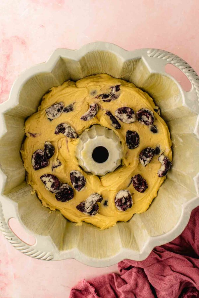Fresh cherries scattered over the first batter layer, kept away from the pan edges in a layered cherry bundt cake