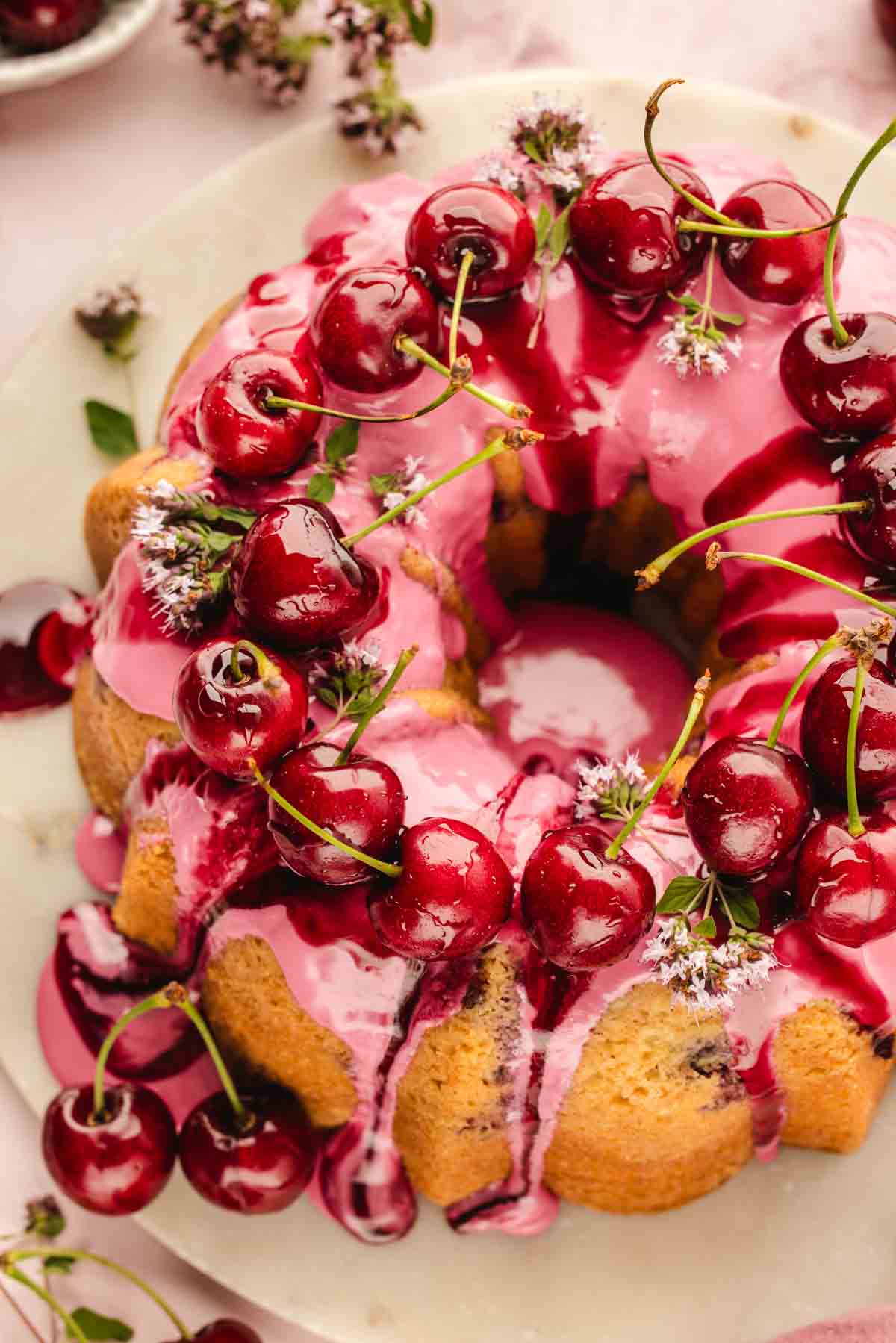 Fresh cherry bundt cake on a cake stand, fully iced and decorated with cherries and flowers