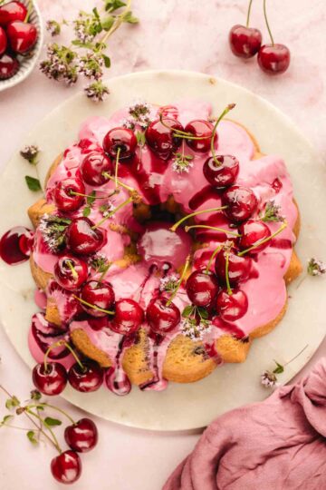 Fresh cherry bundt cake on a cake stand, fully iced and decorated with cherries and flowers