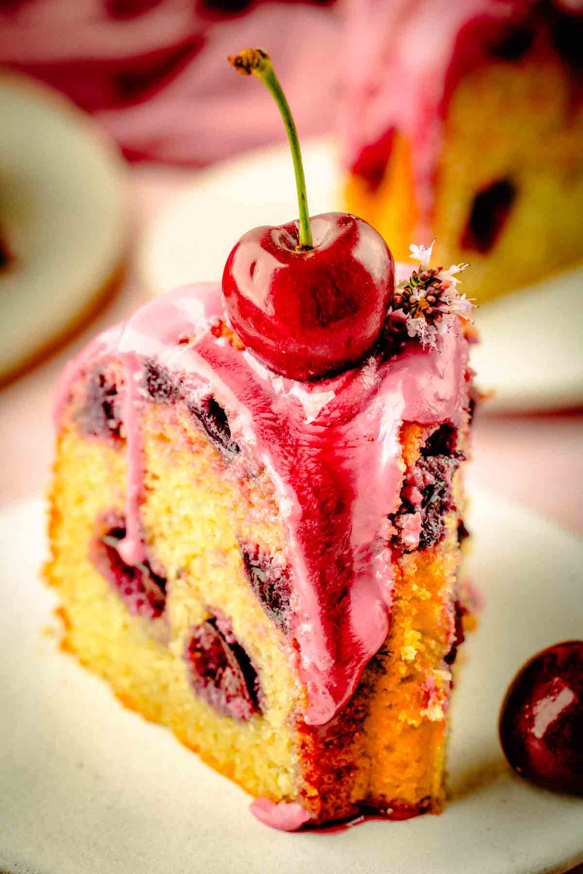 Sliced cherry bundt cake on a plate showing fresh cherries distributed through three layers of crumb
