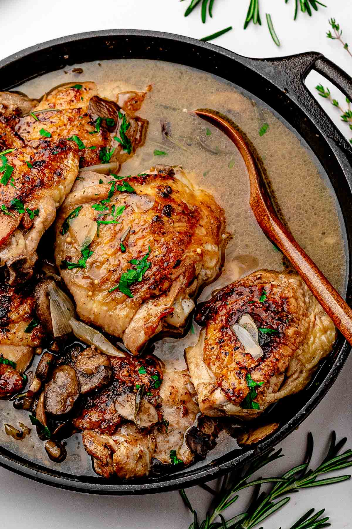 Apple cider braised chicken thighs with mushrooms and shallots in a skillet, glossy sauce spooned over crispy skin