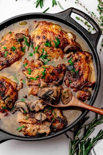 Overhead view of the finished apple cider braised chicken thighs skillet with mushrooms, shallots, and fresh parsley, with skin above the liquid