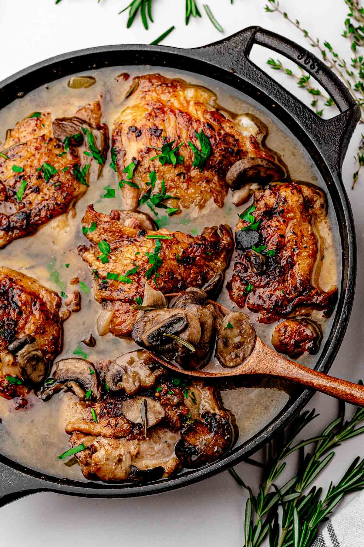 Overhead view of the finished apple cider braised chicken thighs skillet with mushrooms, shallots, and fresh parsley, with skin above the liquid