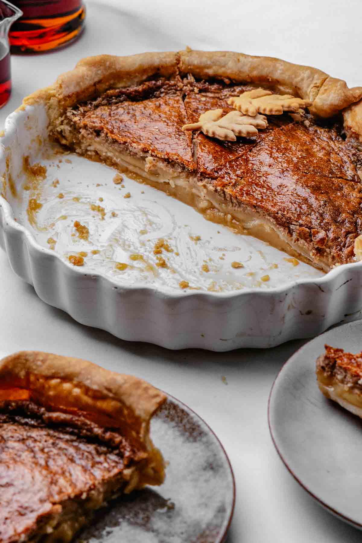 Sliced maple syrup pie showing a soft, custardy center and flaky pie crust Whole maple syrup pie with a golden, glossy top in a store-bought pie crust, cooling on a round pie dish with maple leaf cut outs on top of the pie
