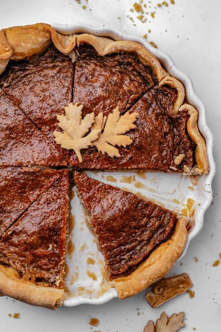 Sliced maple syrup pie showing a soft, custardy center and flaky pie crust Whole maple syrup pie with a golden, glossy top in a store-bought pie crust, cooling on a round pie dish