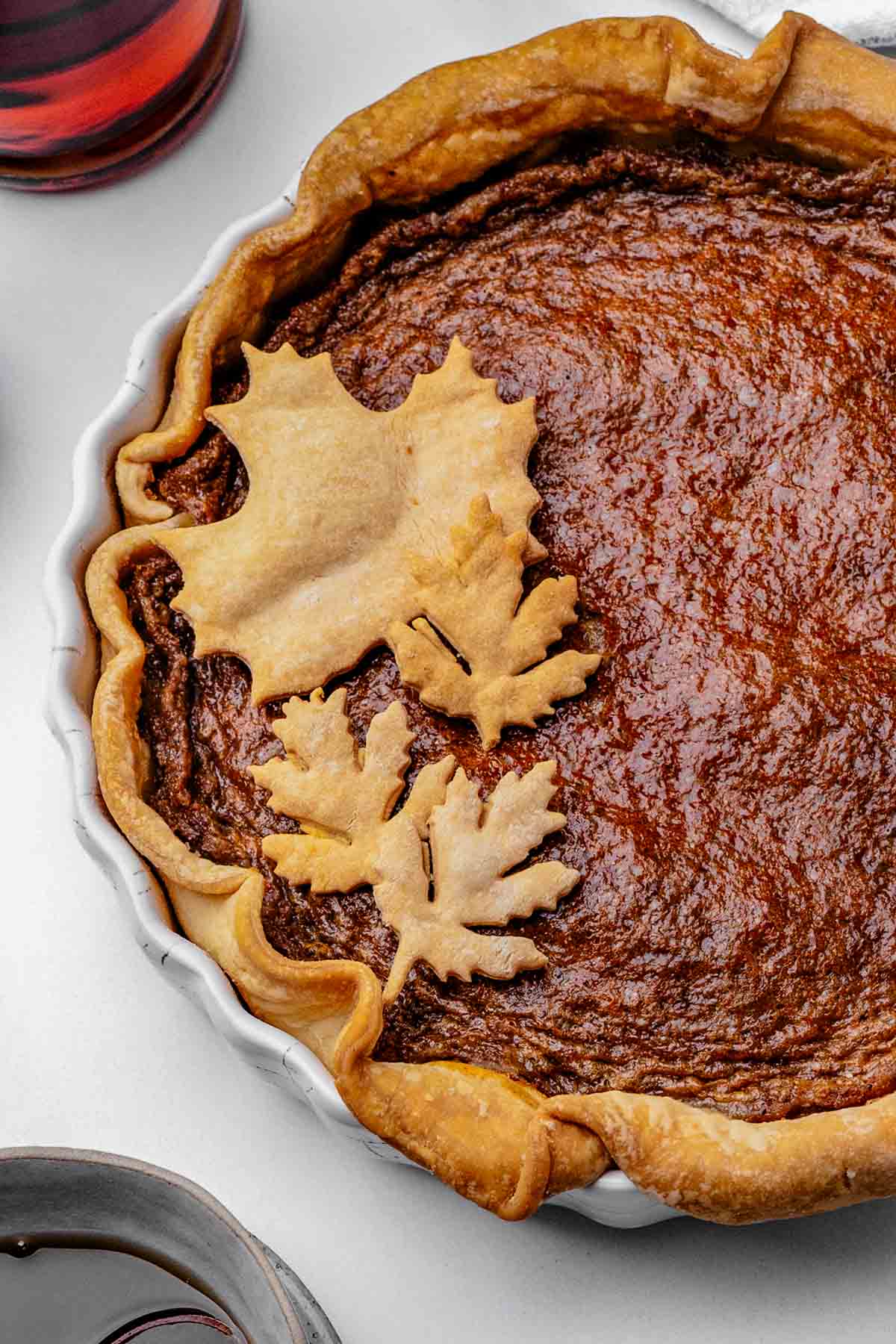 Whole maple syrup pie with a golden, glossy top in a store-bought pie crust, cooling on a round pie dish