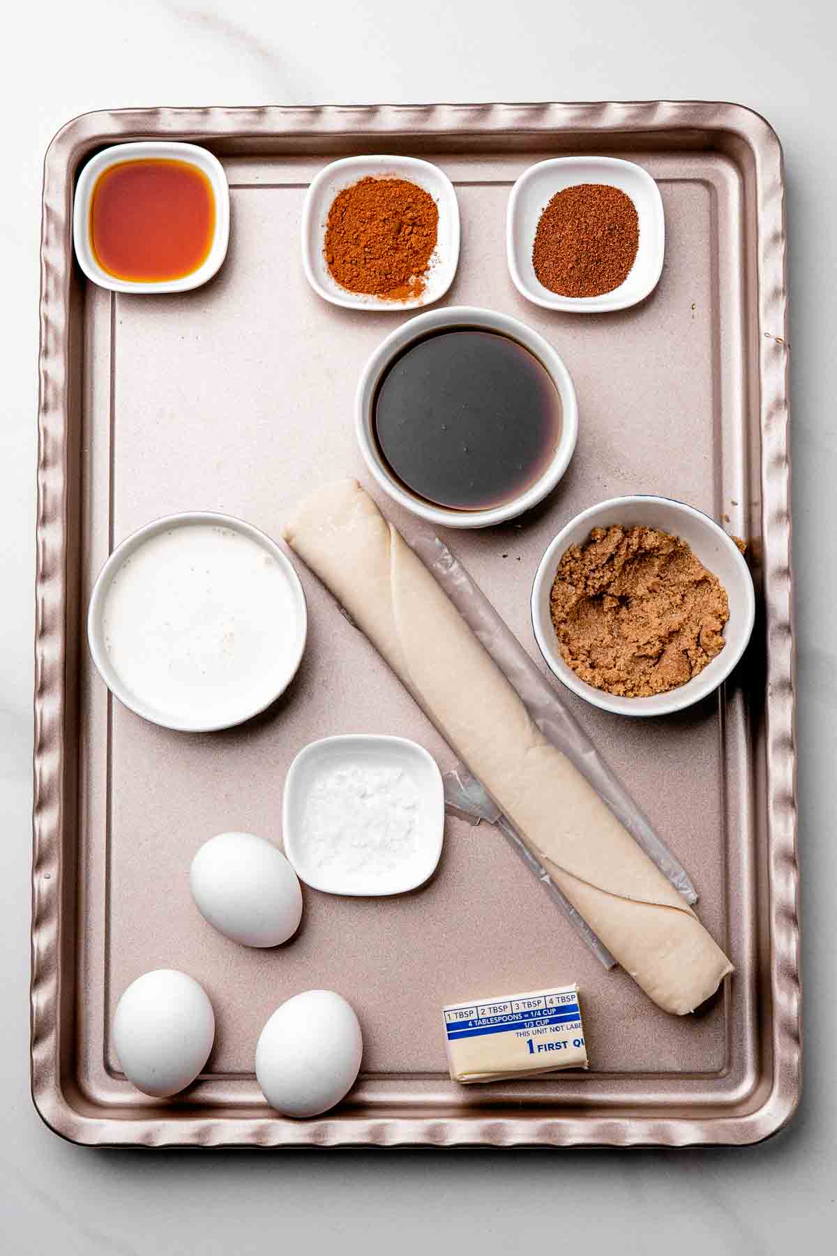 Maple syrup pie ingredients including pure maple syrup, brown sugar, eggs, heavy cream, and melted butter arranged on a tray