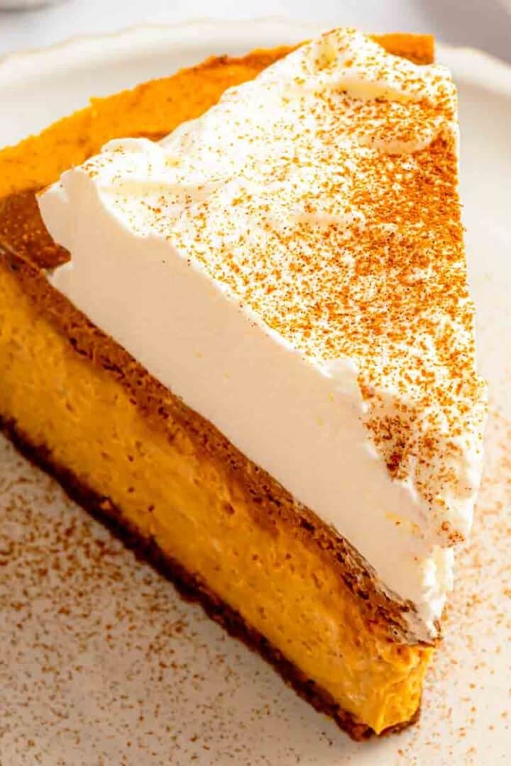 A slice of my pumpkin spice latte cheesecake on a plate, with the gingersnap crust and dark coffee ribbons visible