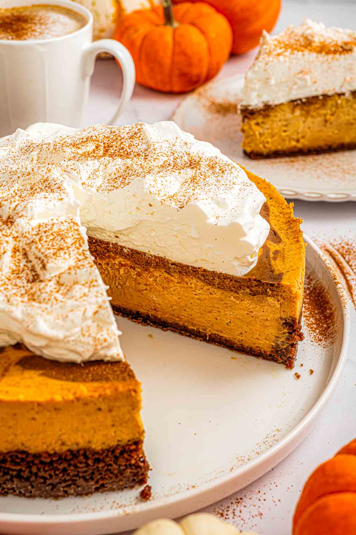 My whole pumpkin spice latte cheesecake on a cake stand, topped with whipped cream and ground cinnamon