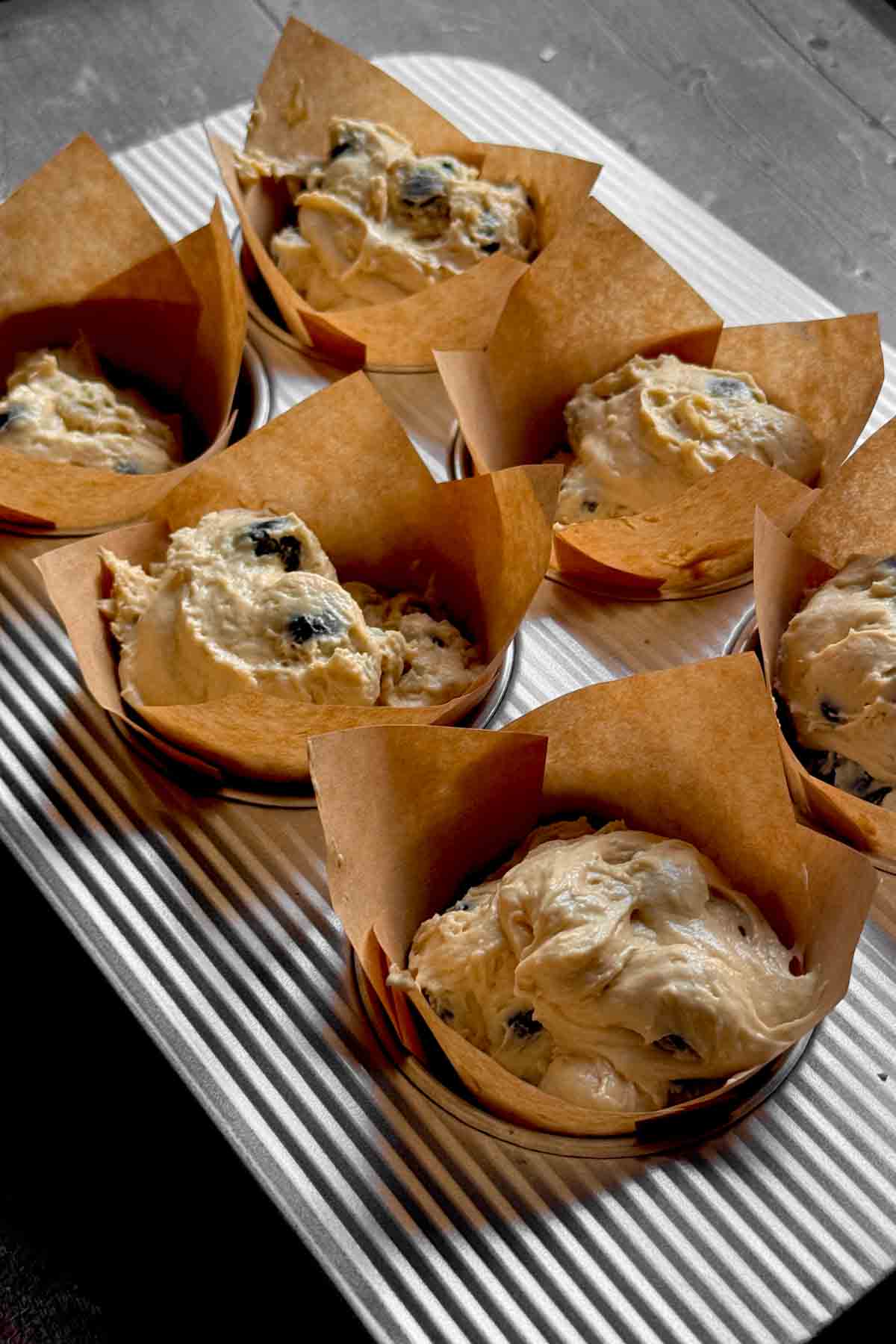 blueberry muffin batter being scooped with an ice cream scooper into tulip lined muffin cups