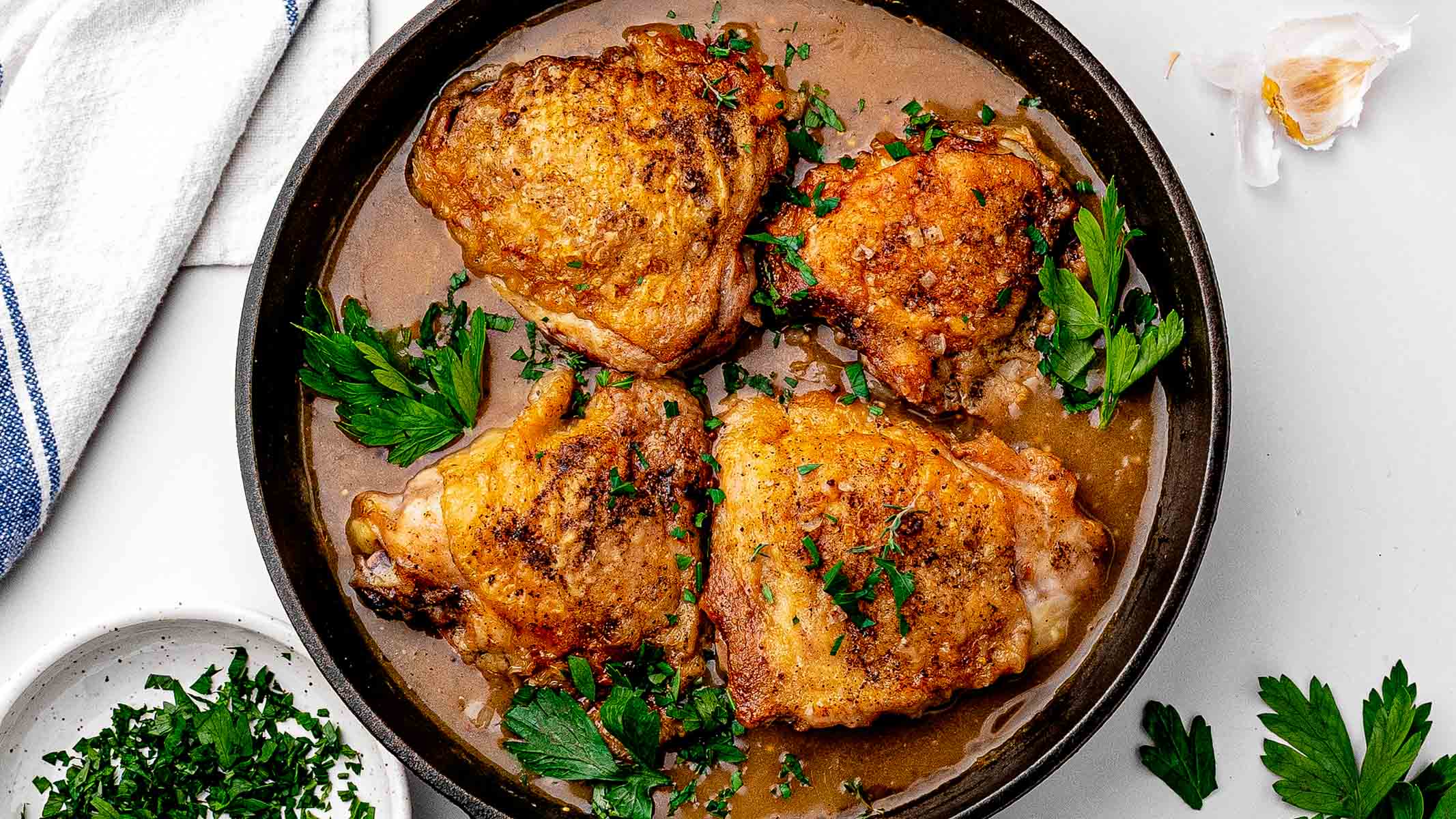 Braised chicken thighs with crispy golden skin in a skillet of glossy beer sauce, sprinkled with parsley