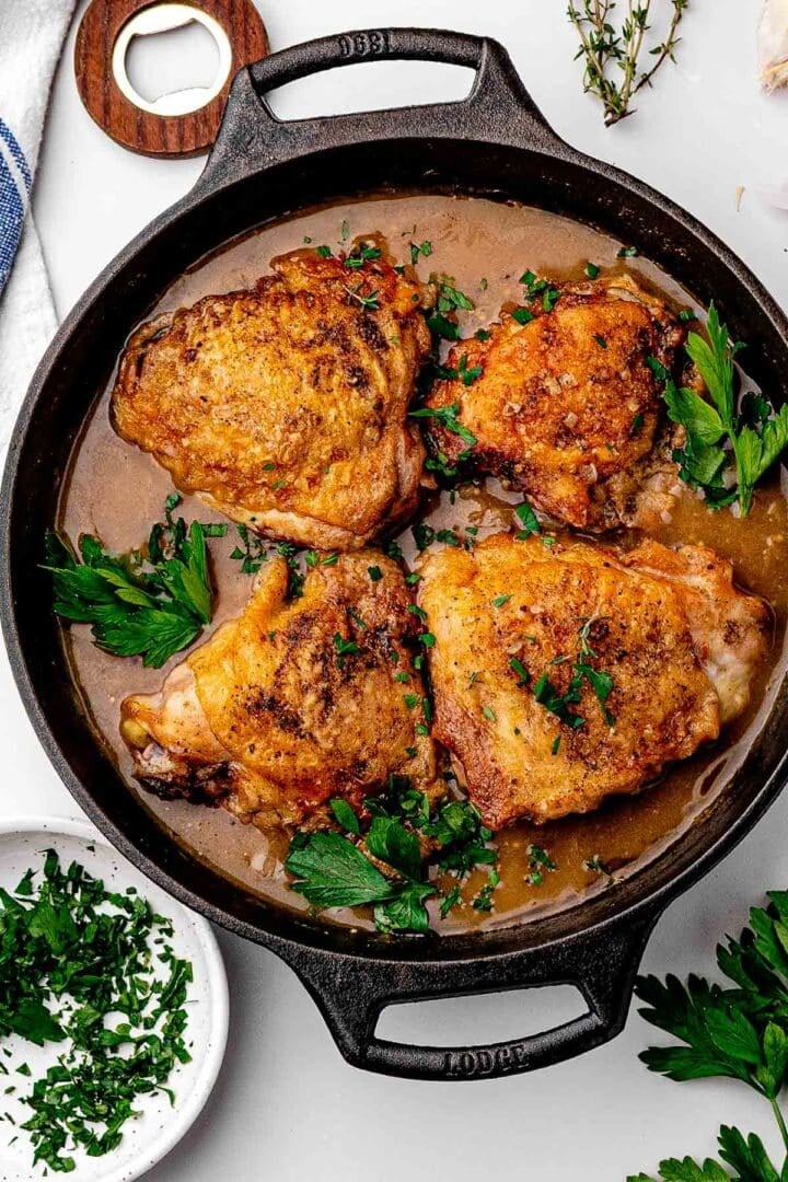 Beer braised chicken thighs in a cast iron skillet with crackly skin above a dark, bubbling sauce