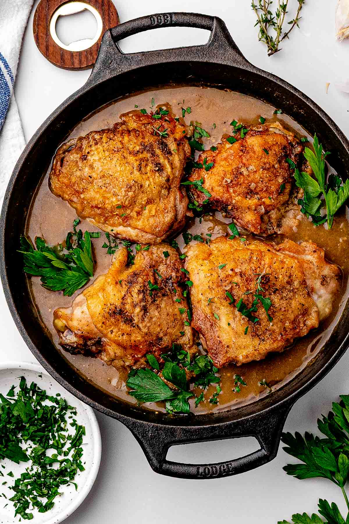 Beer braised chicken thighs in a cast iron skillet with crackly skin above a dark, bubbling sauce