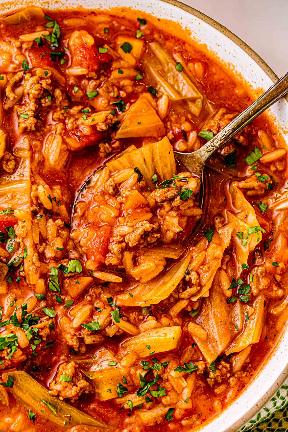 Spoon lifting cabbage roll soup with pork, carrots, and rice from a bowl