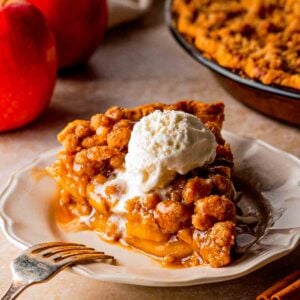 Slice of Dutch caramel apple pie with cinnamon-spiced apples and buttery crumble on a plate.