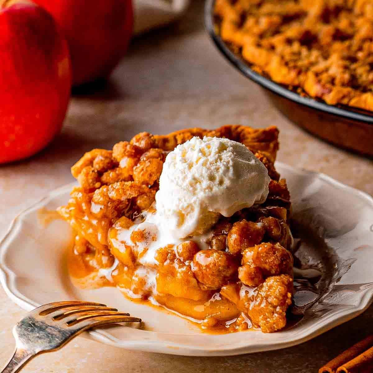 Slice of Dutch caramel apple pie with cinnamon-spiced apples and buttery crumble on a plate.