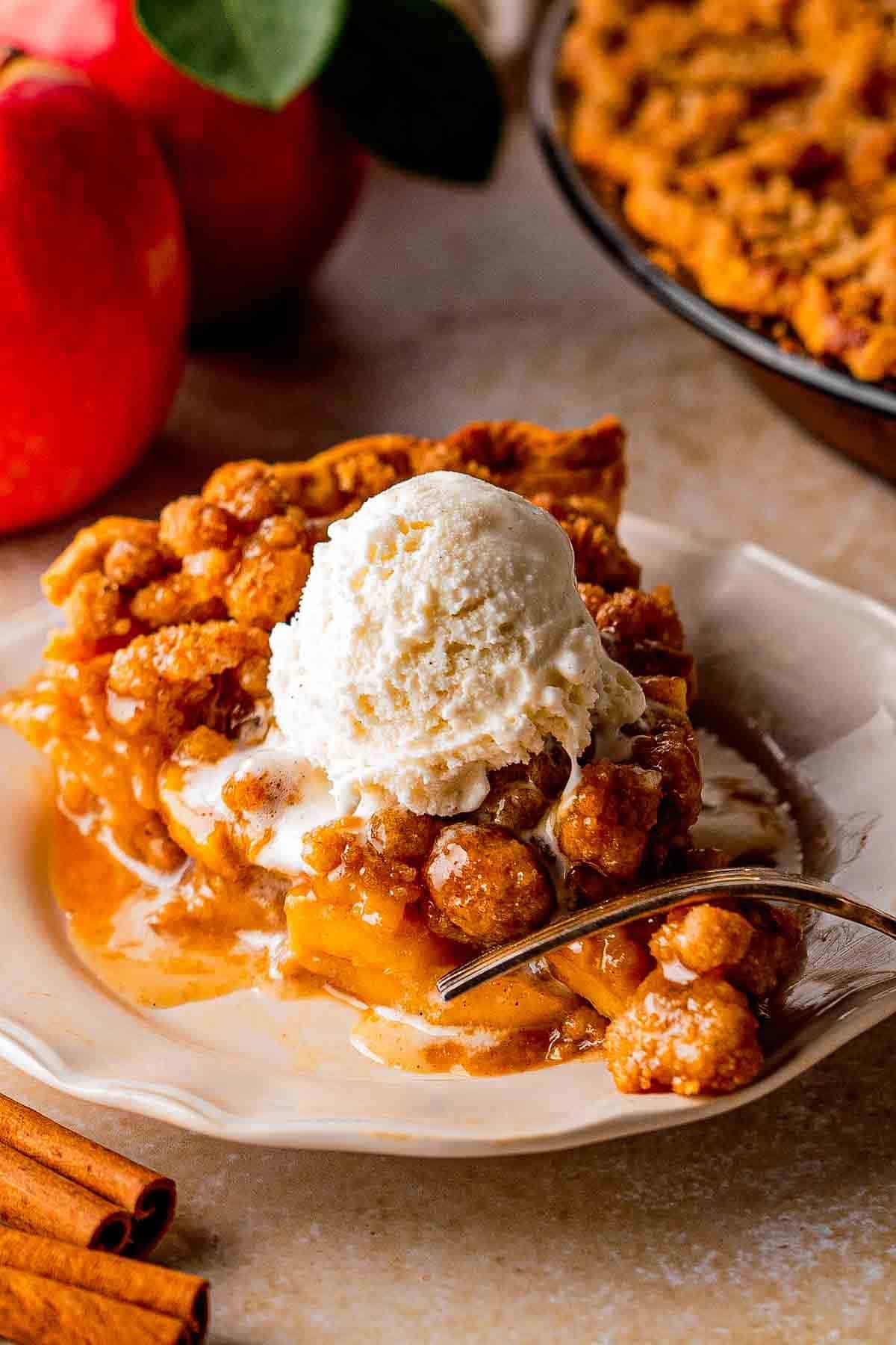 Slice of Dutch caramel apple pie with cinnamon-spiced apples and buttery crumble on a plate.