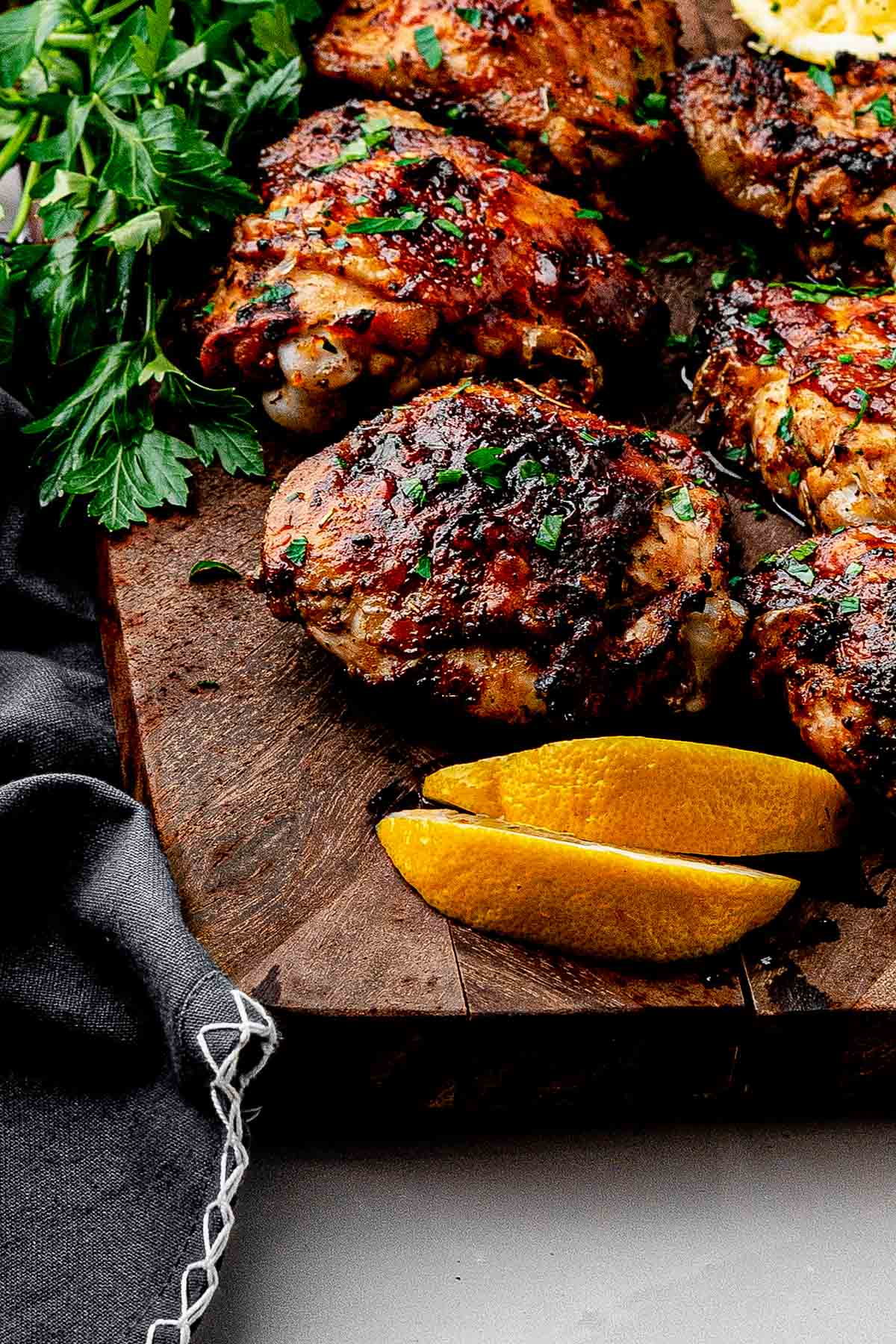 Close up of lemon pepper chicken thighs with homemade lemon pepper rub, parsley and lemon wedges on a cutting board