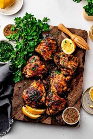 Crispy dry rub chicken thighs with homemade lemon pepper rub on a sheet pan with lemon wedges and parsley