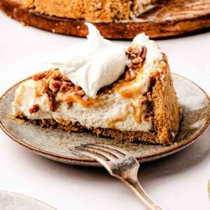 A slice of no-bake pecan pie cheesecake topped with glossy maple-butter pecans on a white cake stand