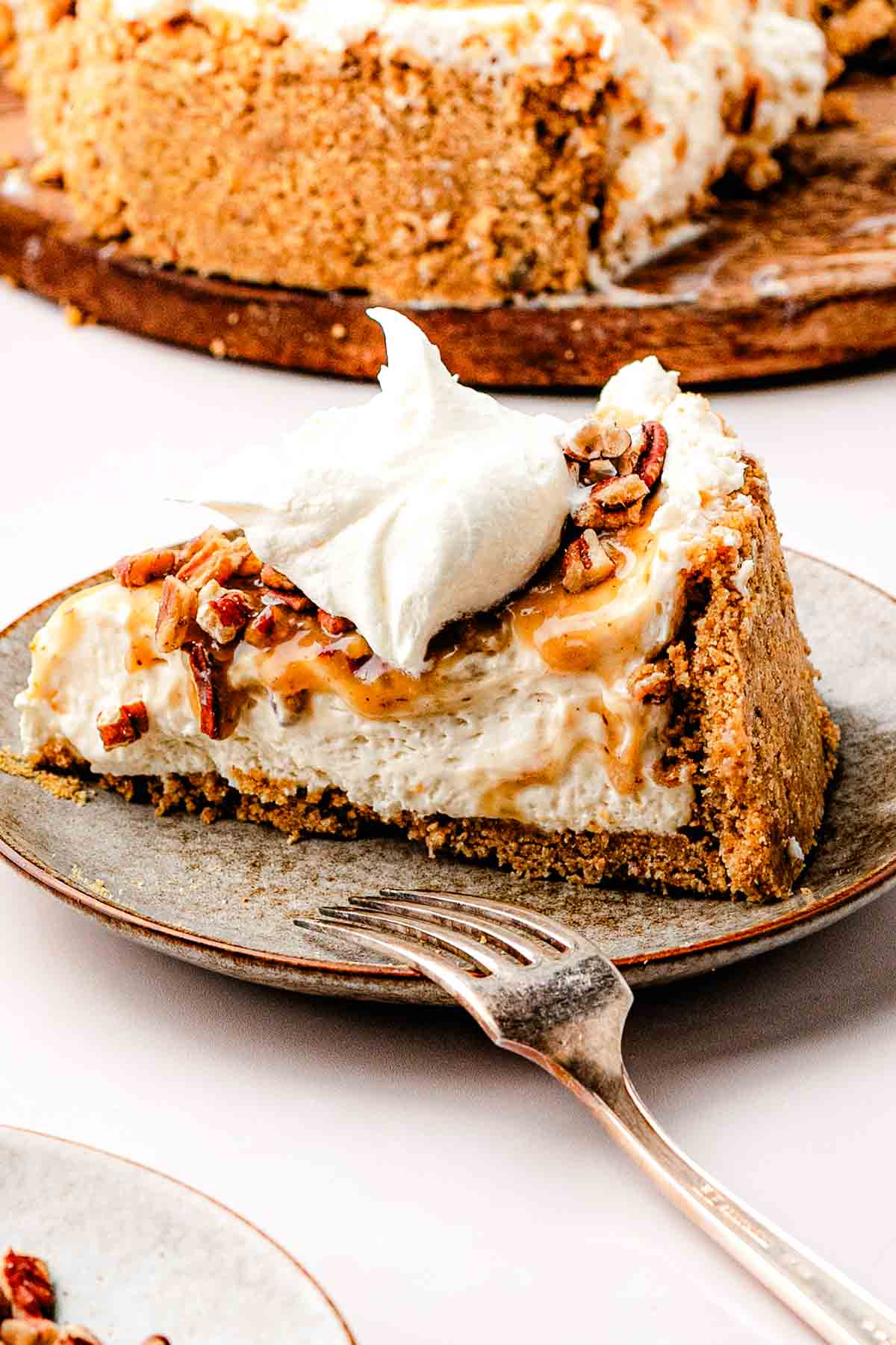  A clean slice of pecan pie cheesecake on a plate, showing the graham-pecan crust and creamy brown sugar filling