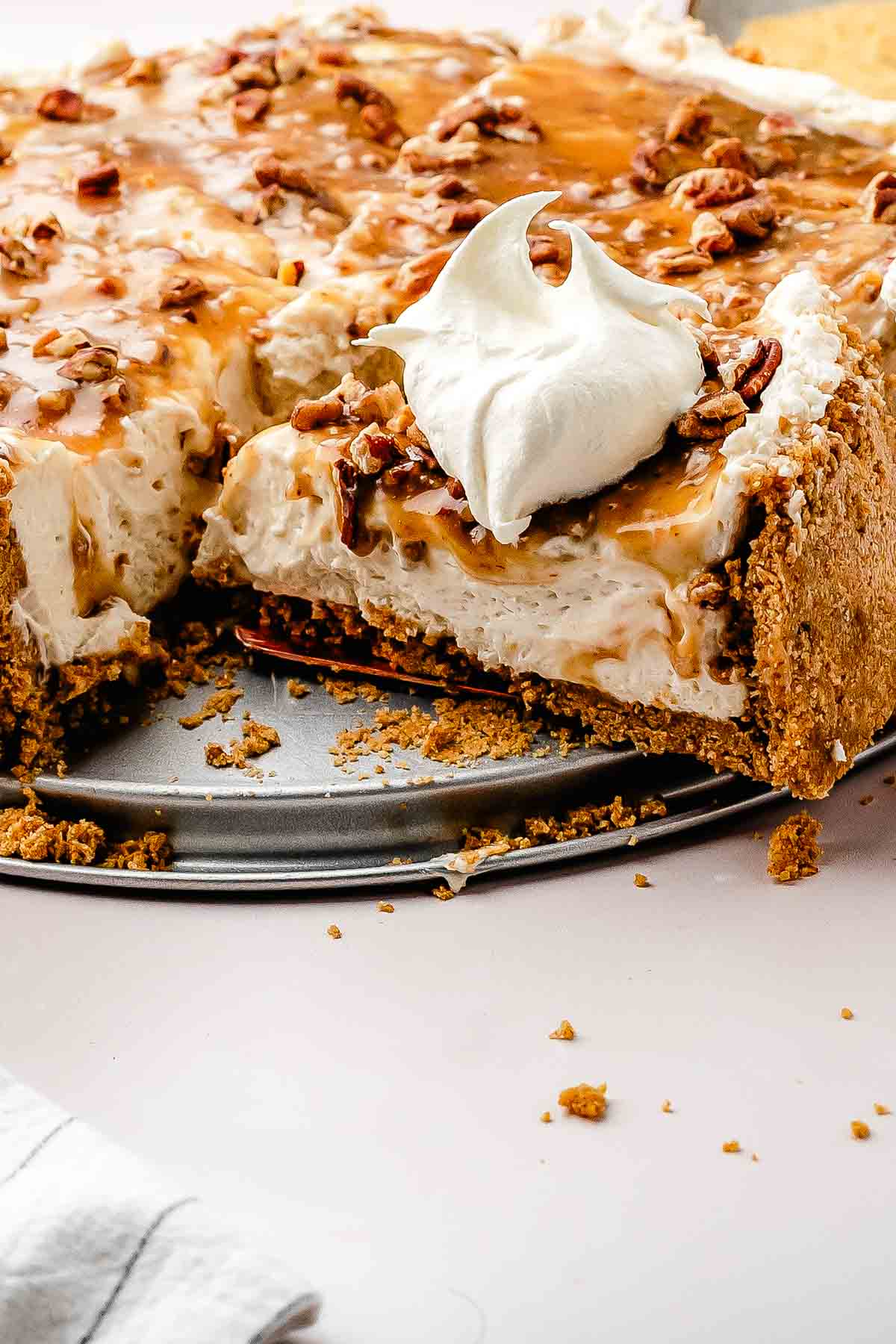 A whole no-bake pecan pie cheesecake topped with glossy maple-butter pecans on a white cake stand