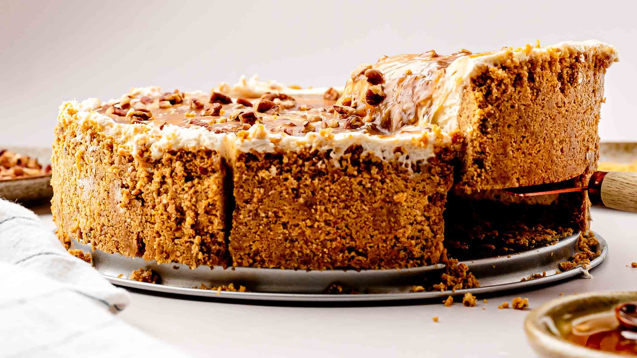 A whole no-bake pecan pie cheesecake topped with glossy maple-butter pecans on a white cake plate