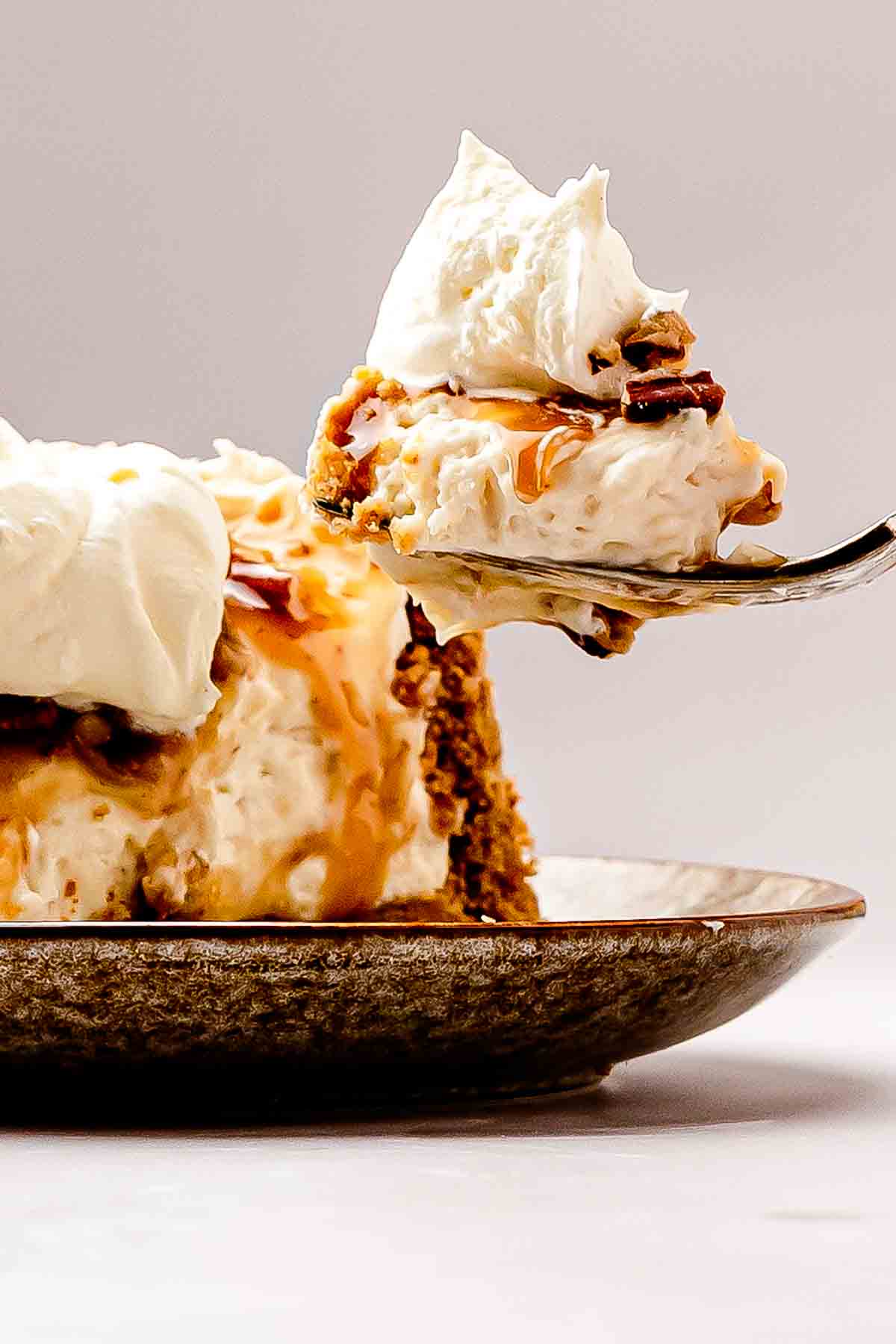 A fork lifting a bite of pecan pie cheesecake with crust, filling, and pecan topping