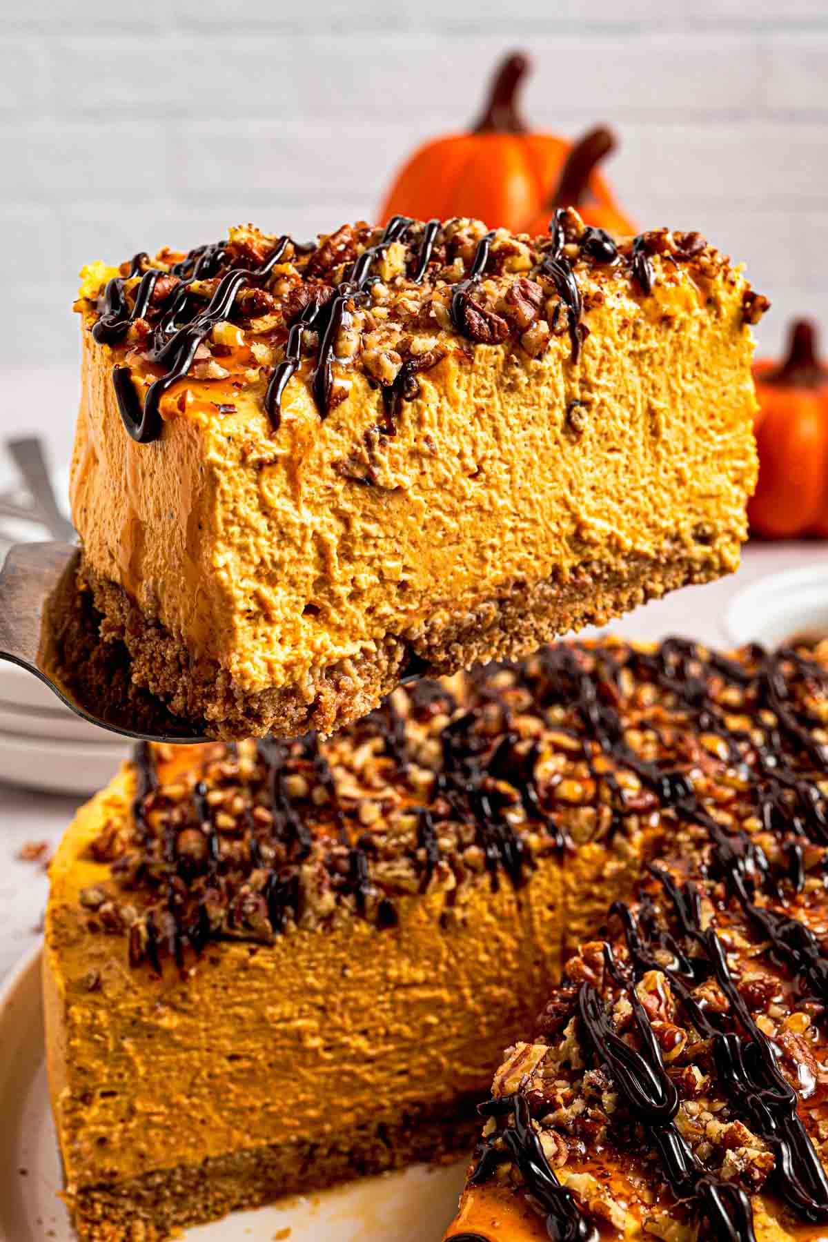 No-bake pumpkin turtle cheesecake topped with pecans, caramel and hot fudge on a cake stand