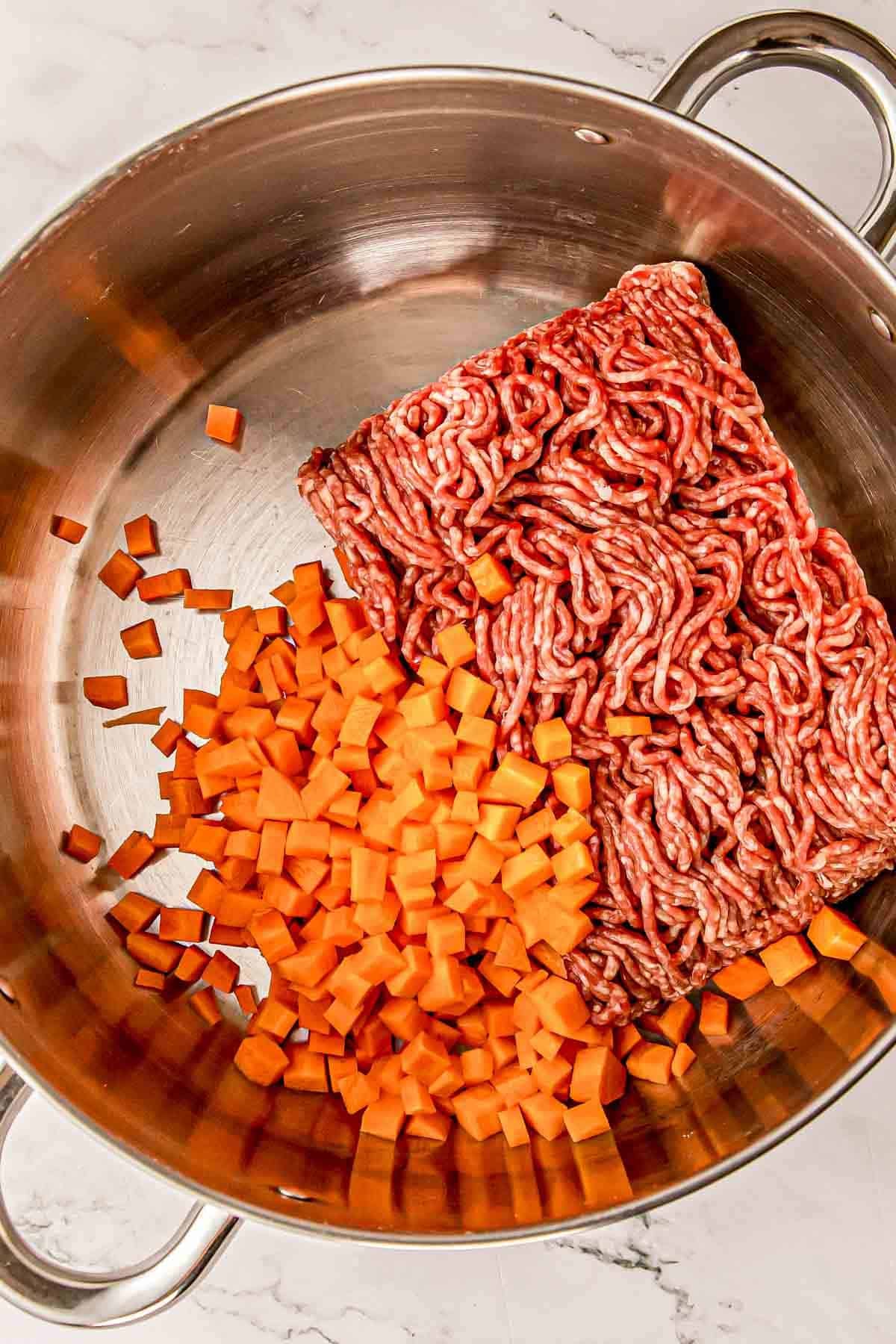 Ground pork and diced carrots browning in a large Dutch oven