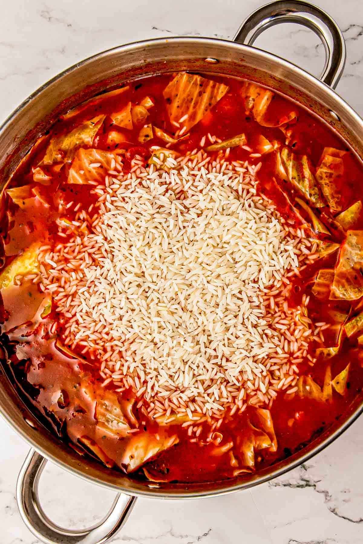 Uncooked long-grain white rice being stirred into the simmering soup