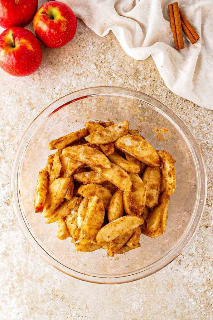 Sliced apples in a mixing bowl with sugar, flour, cinnamon, and nutmeg.
Apple slices tossed with the cinnamon-sugar filling mixture.