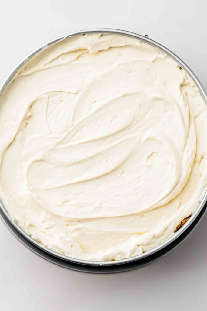 Spreading filling: Spreading the cheesecake filling over the chilled crust with an offset spatula