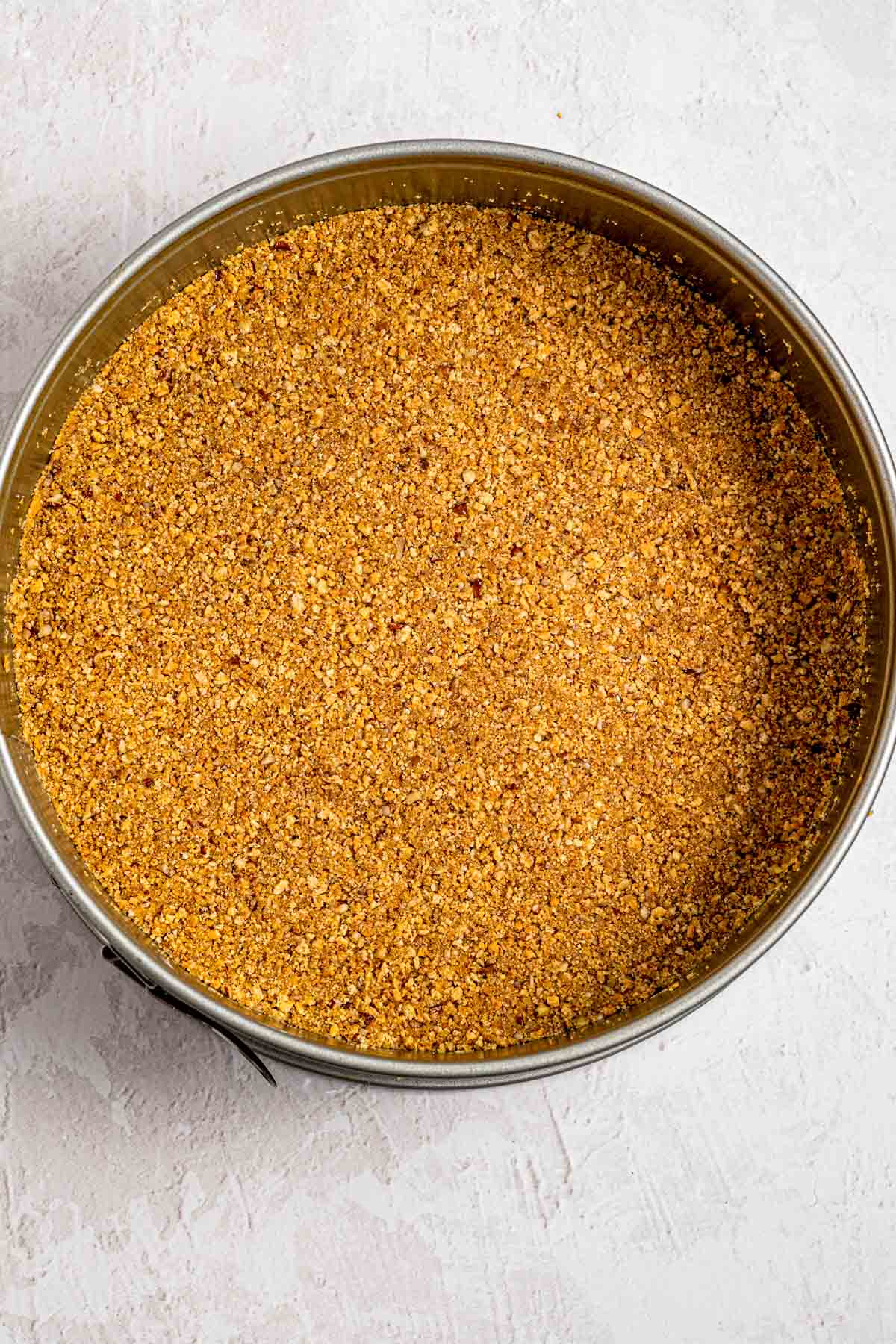 Pressing graham cracker pecan crumbs into a springform pan with the bottom of a measuring cup