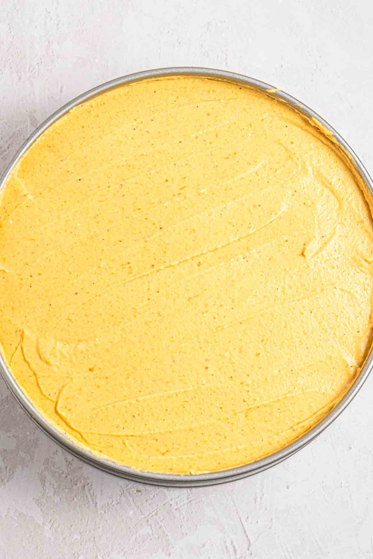 Spreading pumpkin cheesecake filling over a frozen crust with an offset spatula