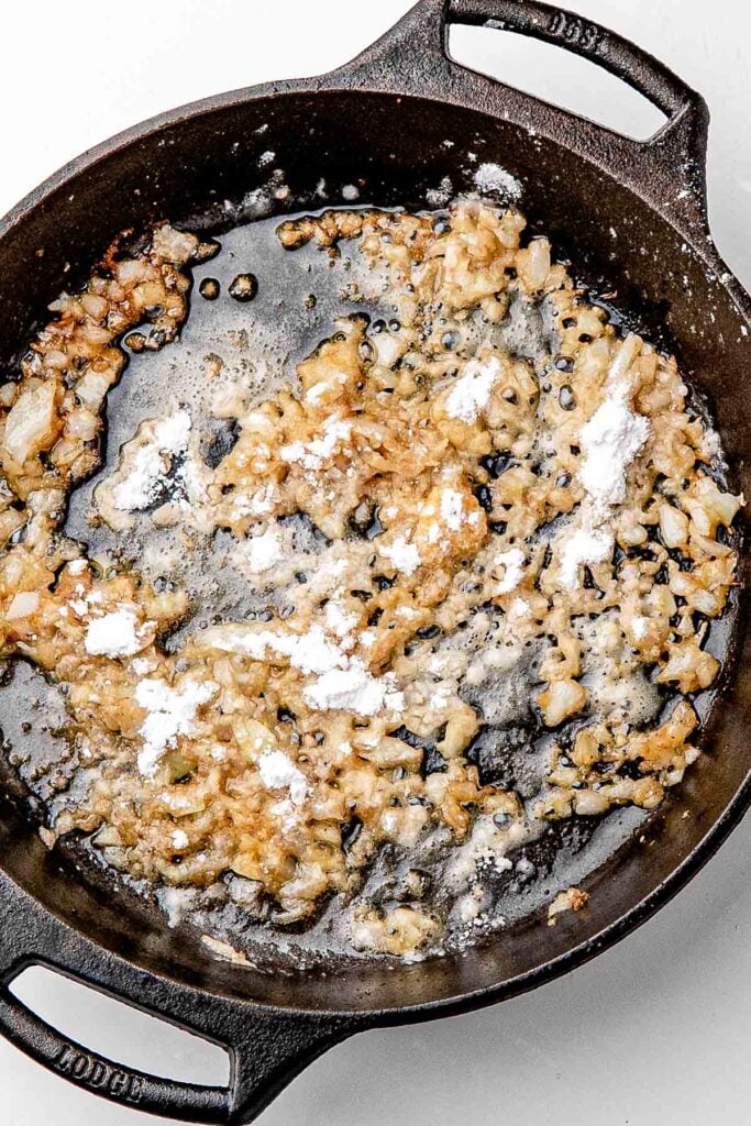 Sliced yellow onions softening in the skillet with browned bits left from the chicken thighs