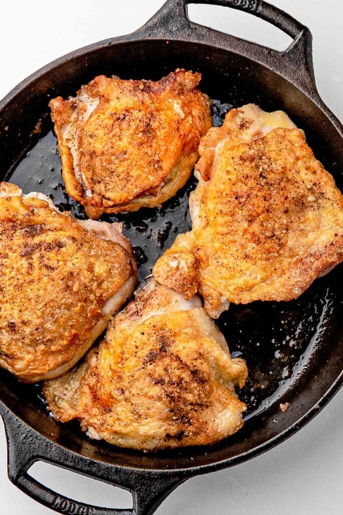 Chicken thighs searing skin-side down in a hot skillet until deep golden brown