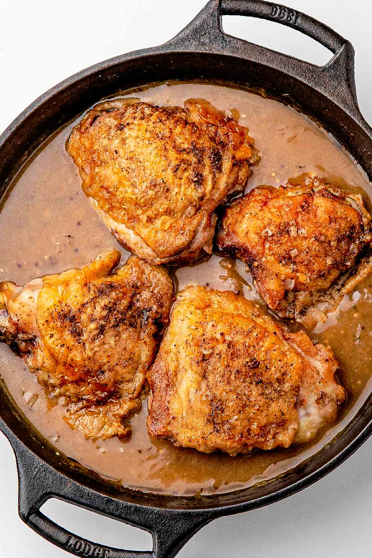 Braised chicken thighs fresh from the oven with golden skin above the bubbling beer sauce