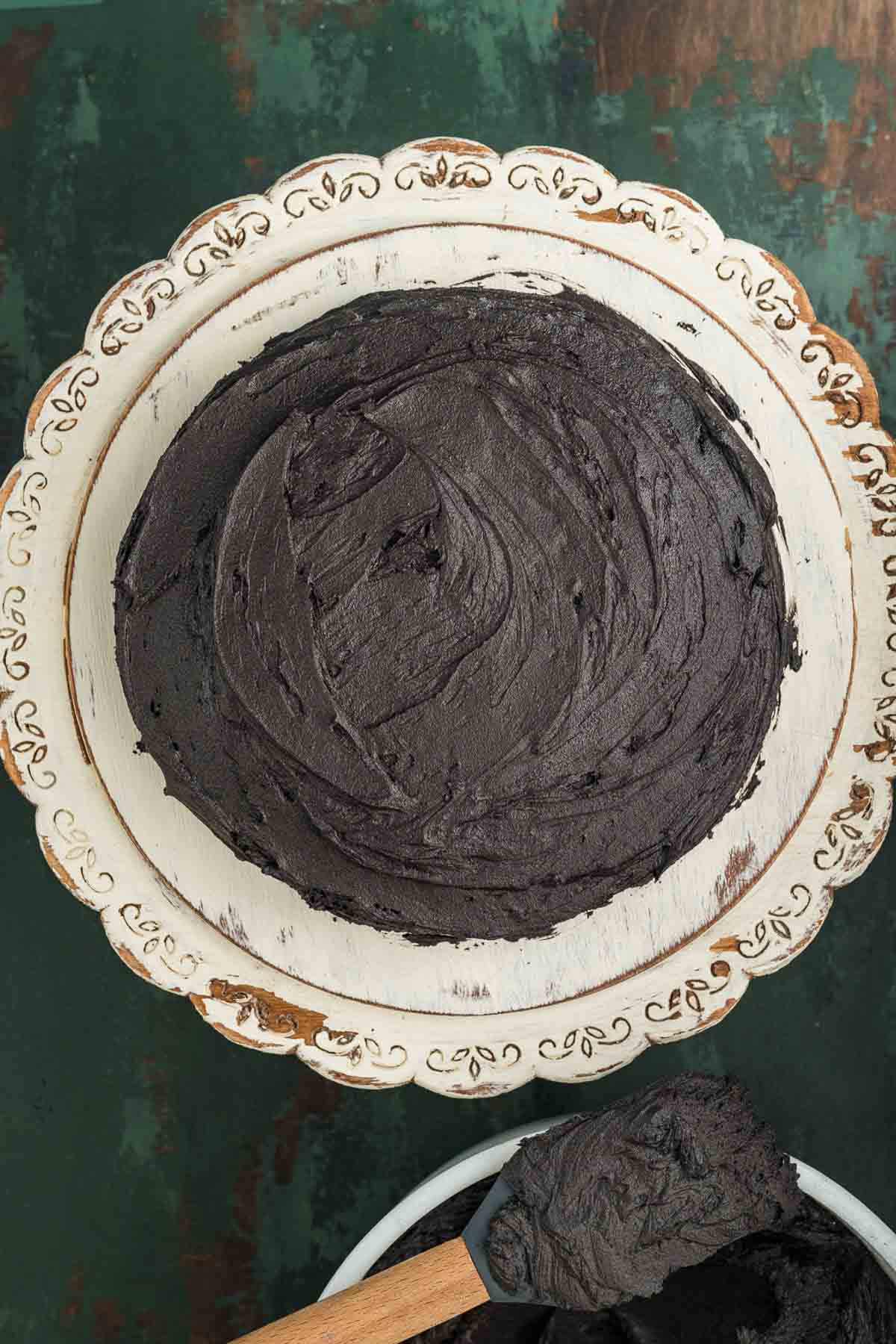 First black cake layer on a plate spread with a cup of black cocoa buttercream
