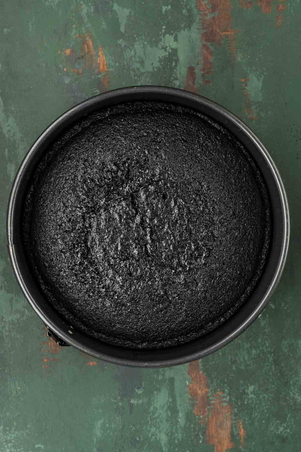 Black cake batter divided evenly among three parchment-lined cake pans