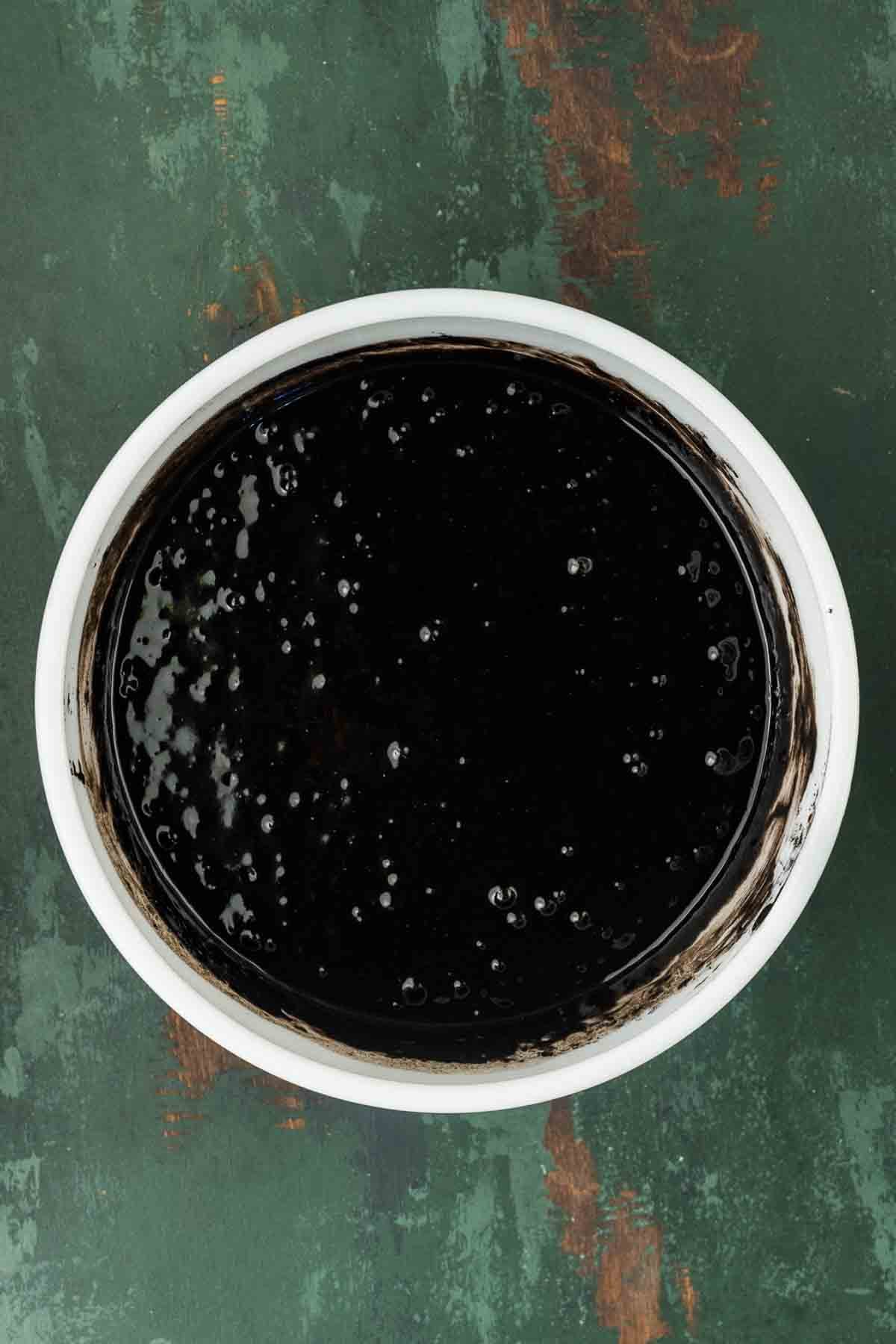 Dry black cocoa mixture being added to the wet ingredients in a mixing bowl