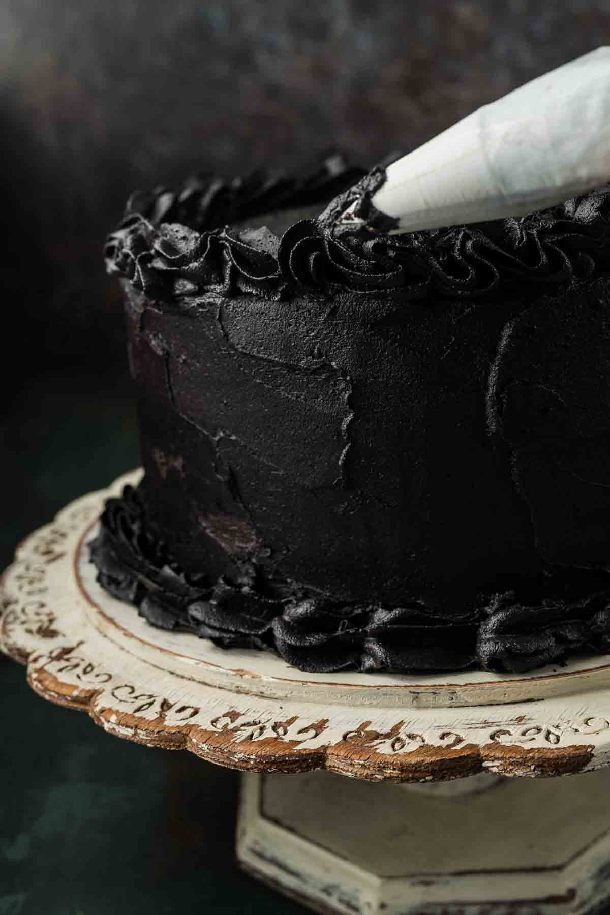 Offset spatula smoothing black cocoa buttercream over the top of the cake