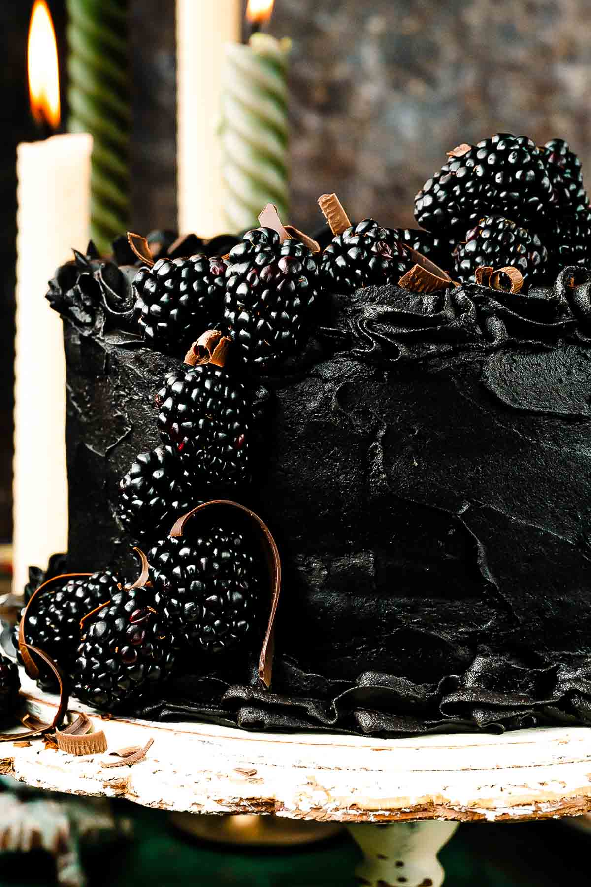 Side view of black velvet cake with piped buttercream swirls and blackberries