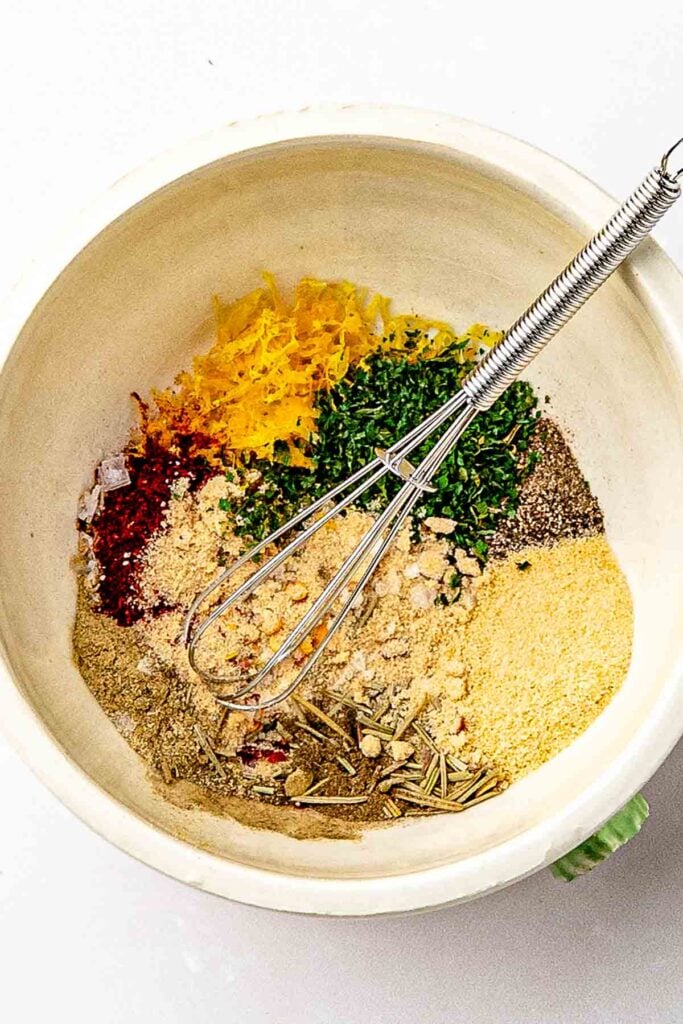 Ingredients for homemade lemon pepper rub: paprika, oregano, thyme, rosemary and lemon zest in the bowl