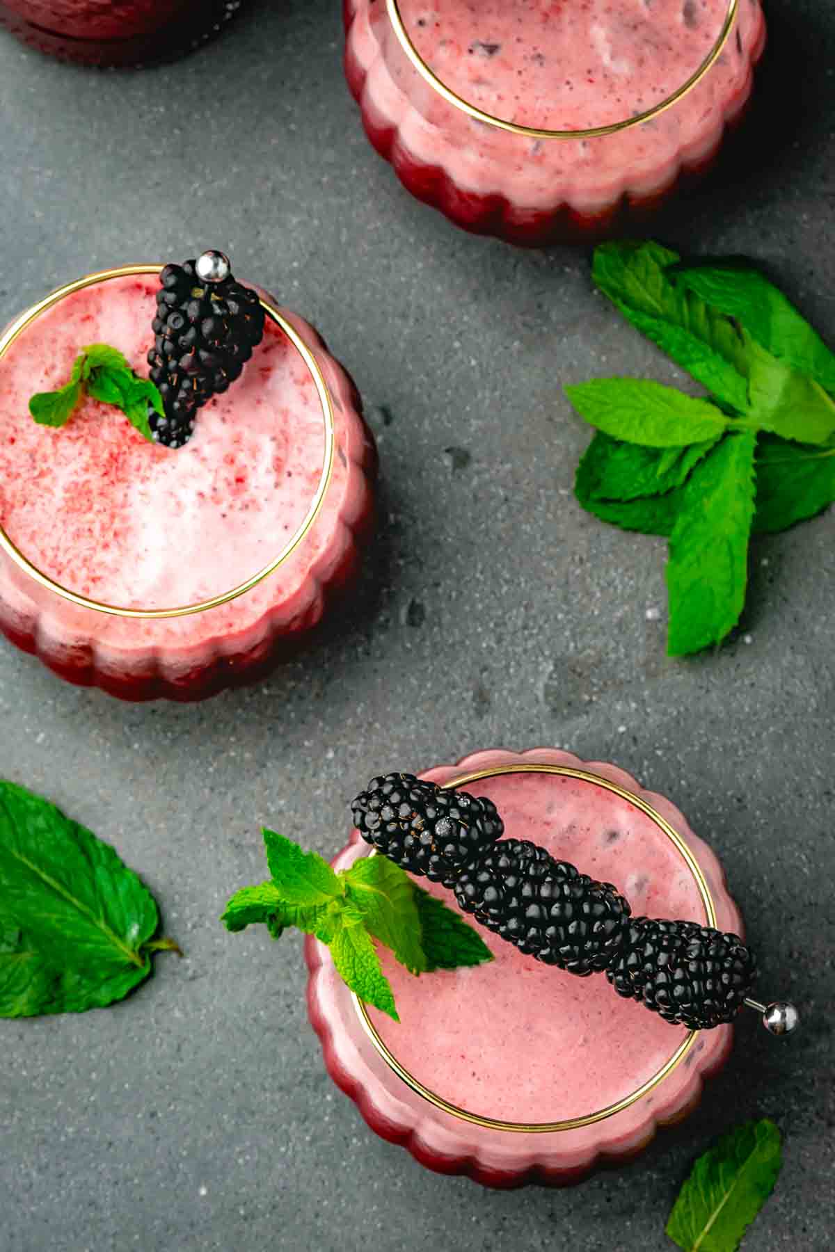 Three pumpkin-style glasses of purple blackberry mocktail garnished with blackberries and fresh mint