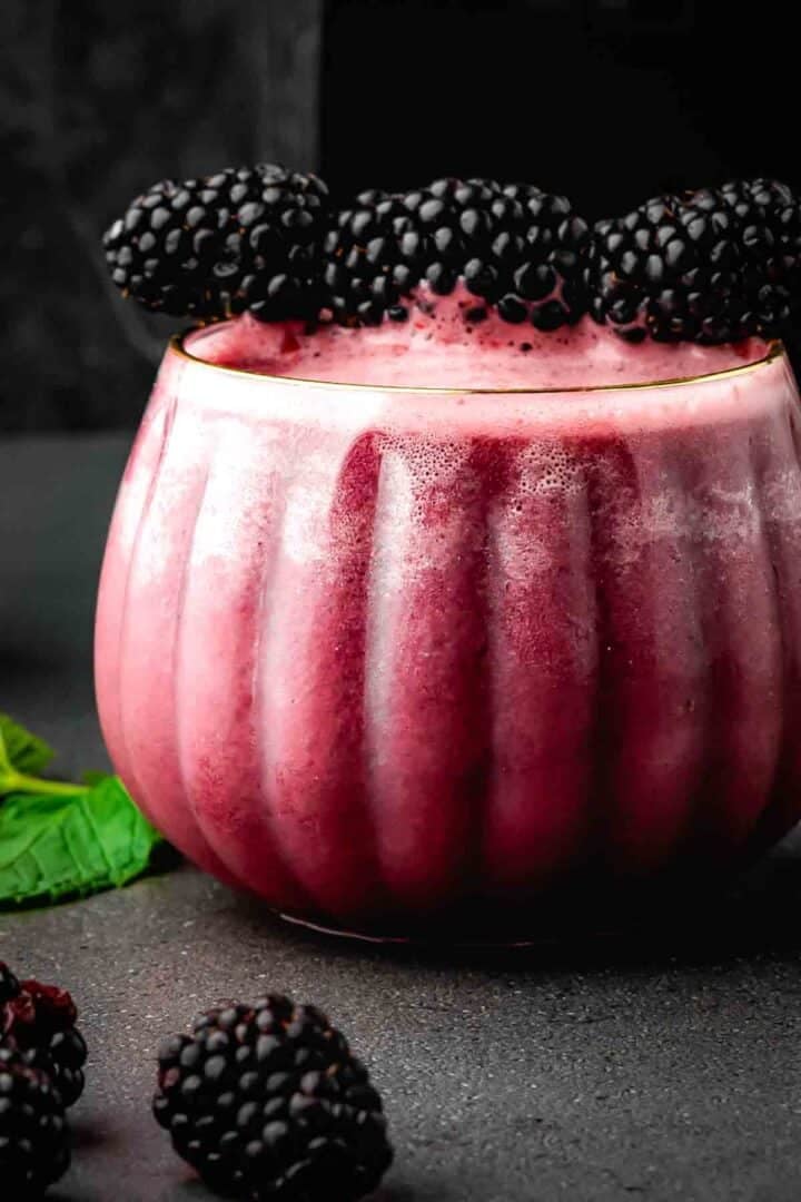 Deep purple blackberry Halloween drink with bubbles, ice, and a mint sprig in a pumpkin-shaped glass
