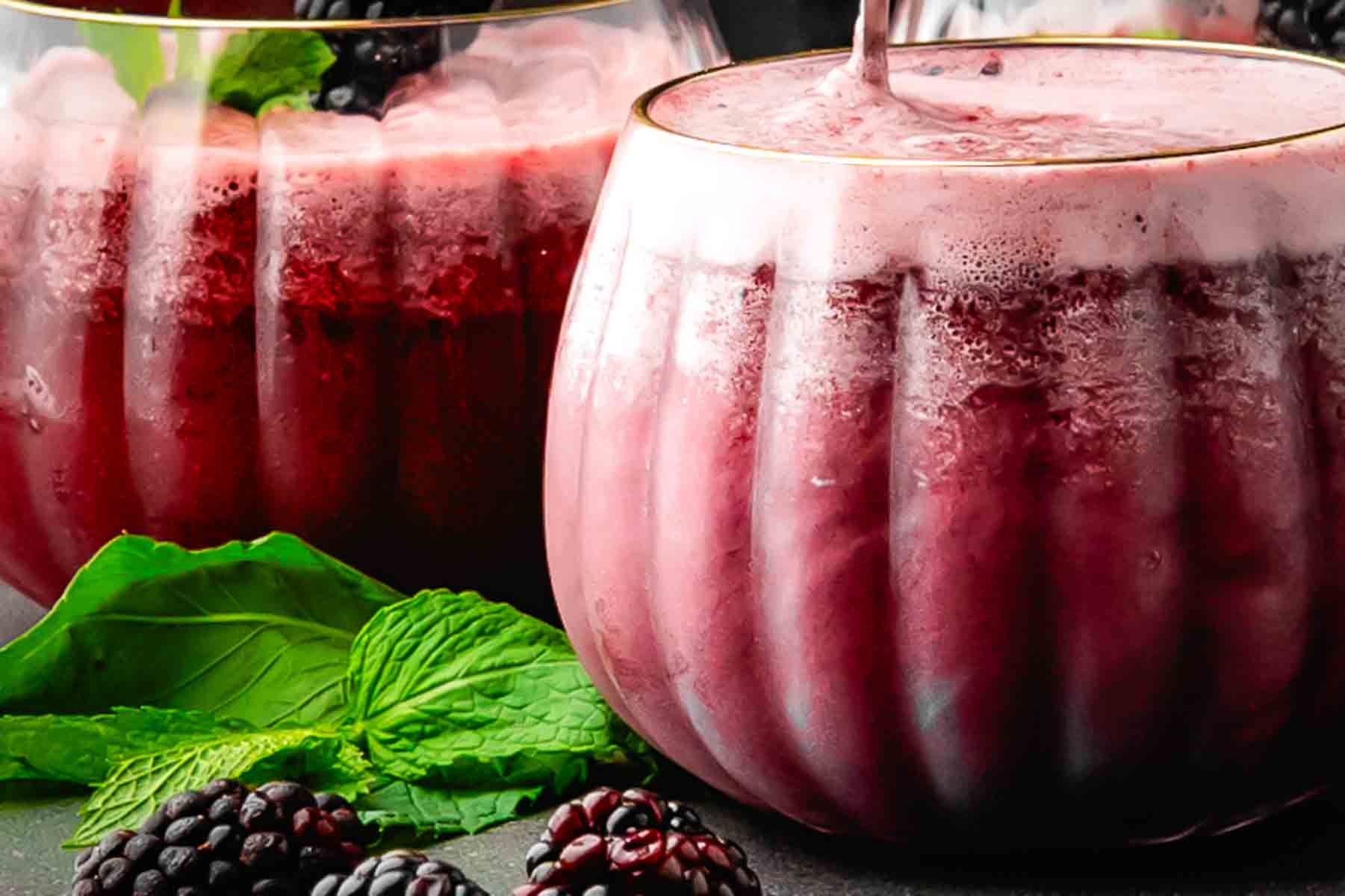 Deep burgundy blackberry Halloween drink with bubbles, ice, and a mint sprig in a pumpkin-shaped glass