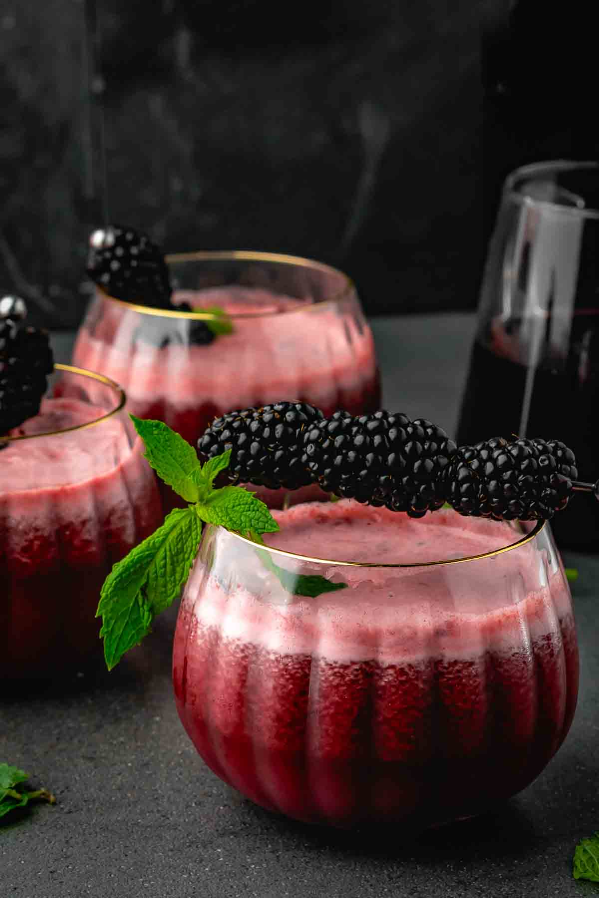 Two pumpkin-style glasses of burgundy blackberry mocktail garnished with blackberries and fresh mint