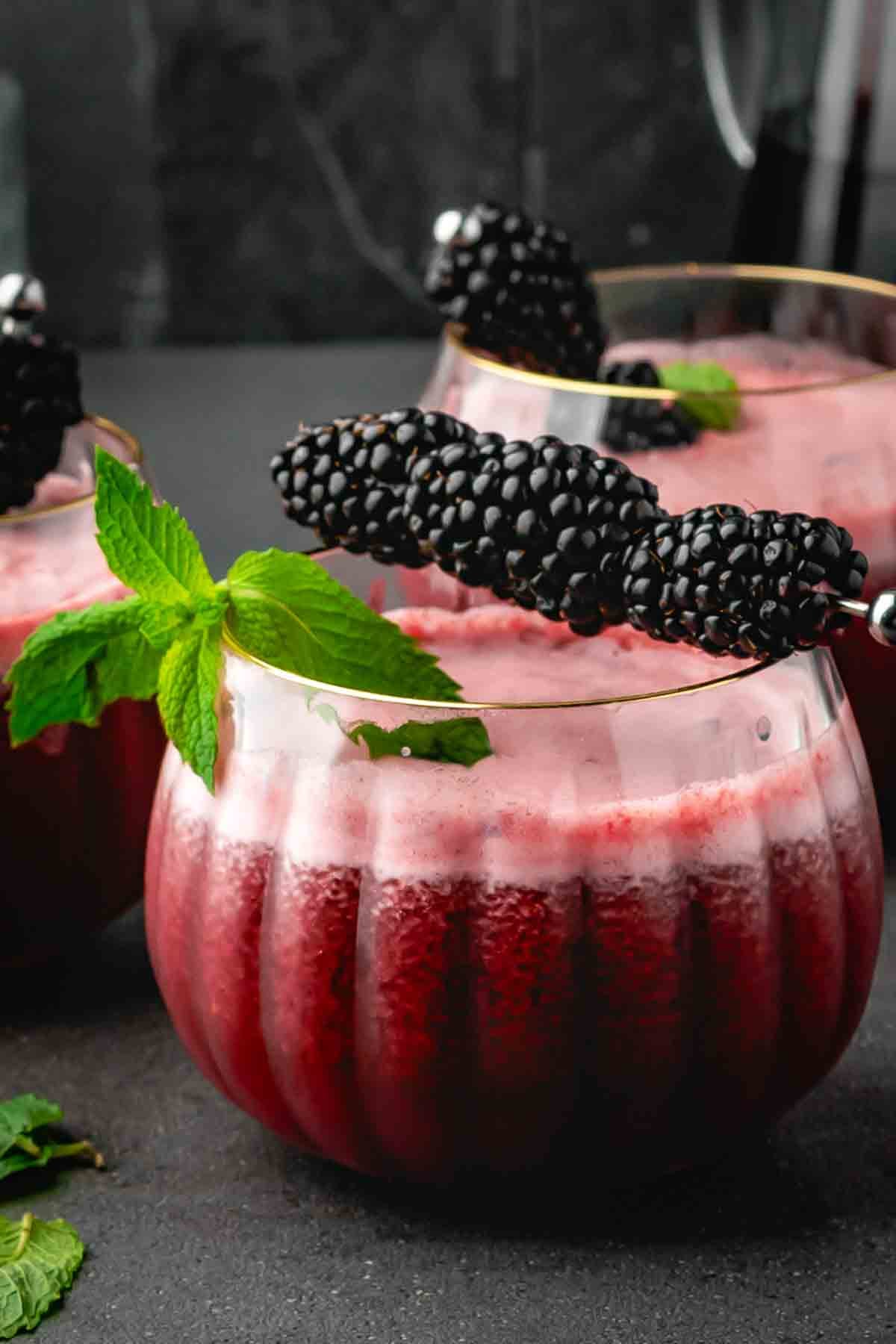 Two pumpkin-style glasses of purple blackberry mocktail garnished with blackberries and fresh mint
